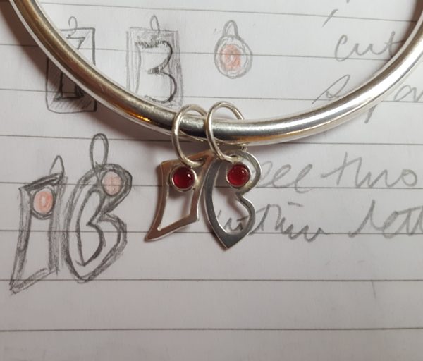 Silver bangle with rubies compared with initial drawing
