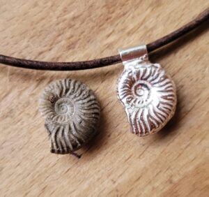 A silver ammonite next to the original it has been cast from.