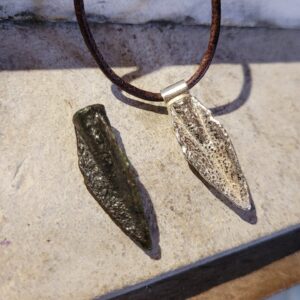 Arrow head sitting next to version cast in silver on a leather cord.