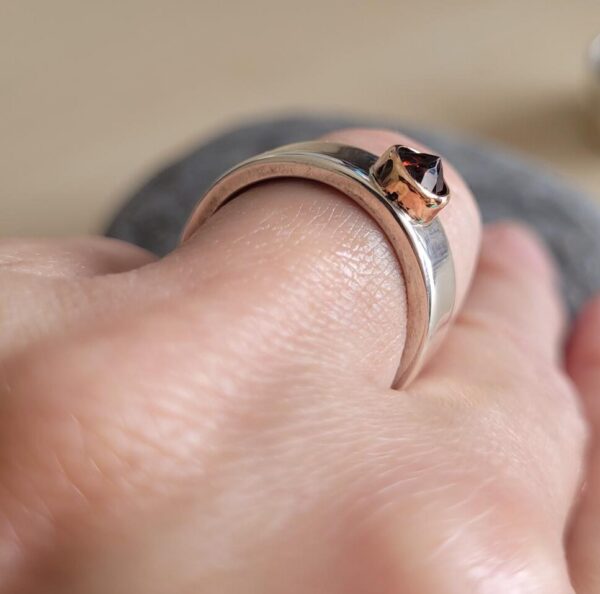 Silver ring with reverse-set red garnet in a rose gold setting.