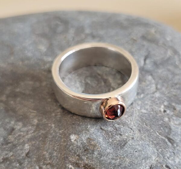 Silver ring with reverse-set red garnet in a rose gold setting.